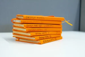 A stack of 7 orange notebooks labeled "Design Notes"